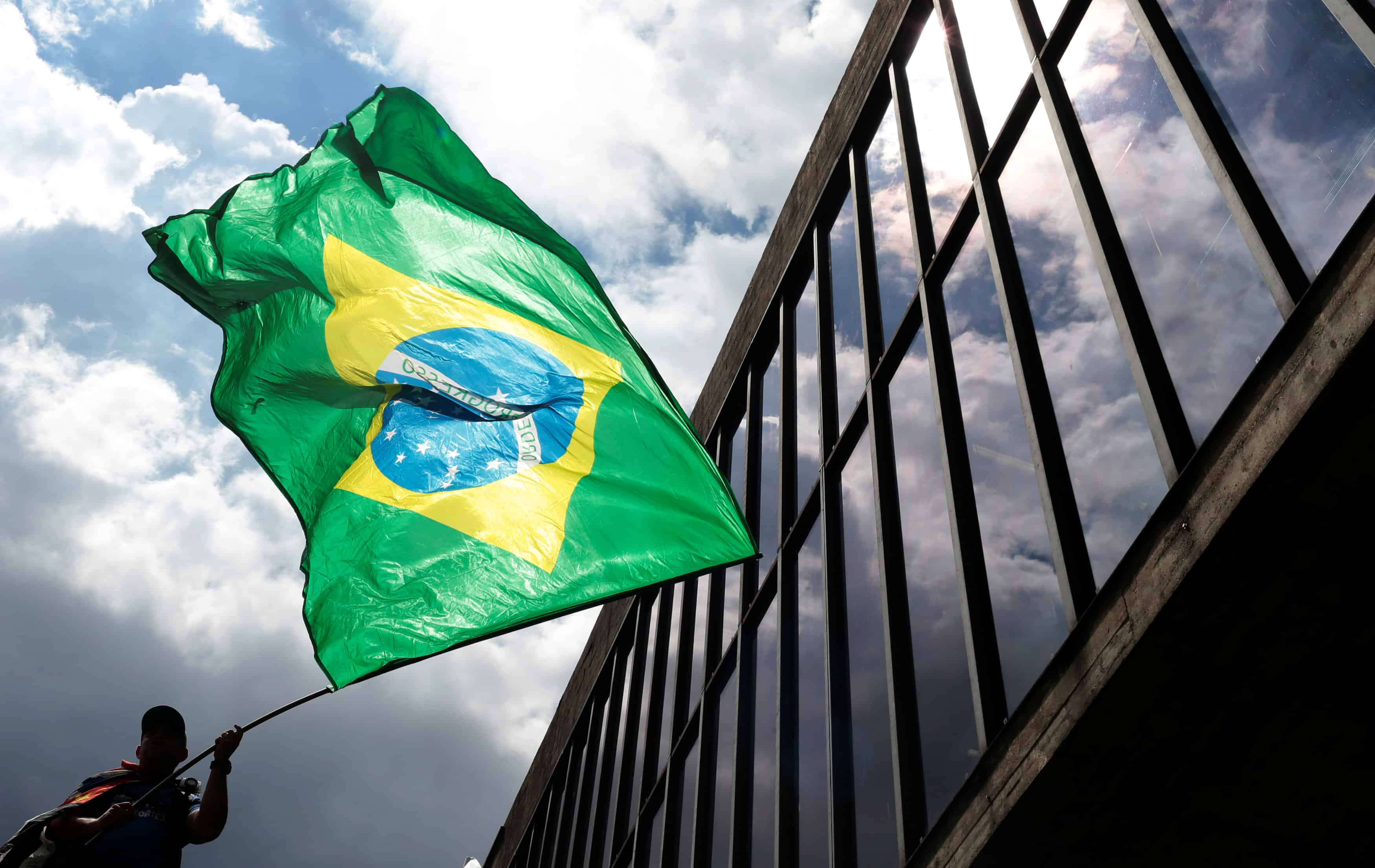 Na imagem temos a silhueta de um homem segurando a bandeira do Brasil.