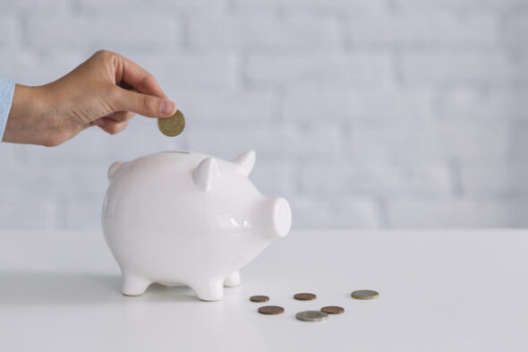 foto de cofre de porquinho branco, com pessoa inserindo moeda