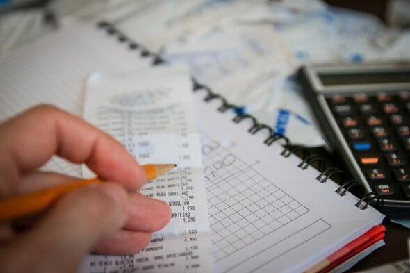 pessoa fazendo cálculo, com folhas, notas fiscais e calculadora - disciplina financeira