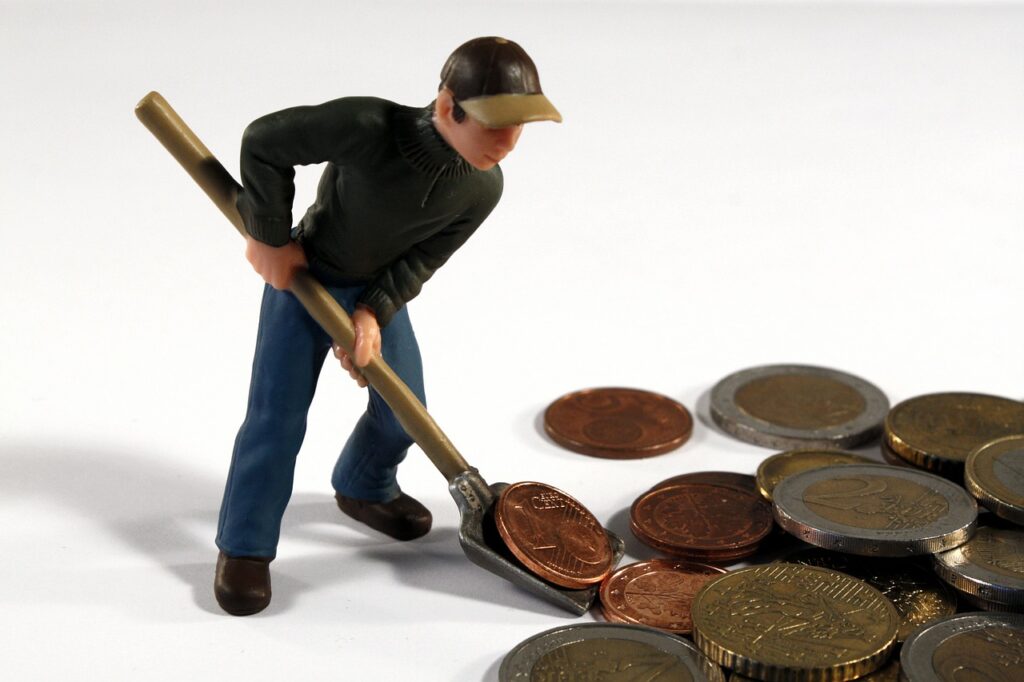 Imagem mostra boneco juntando moedas com uma pá, representando ativos financeiros.