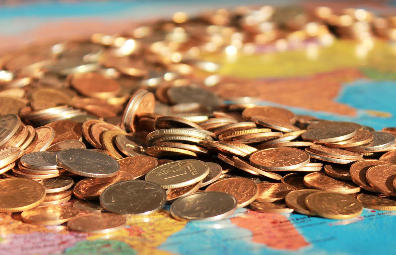 Imagem mostra muitas moedas em cima do mapa mundi, representando o poder de compra corroído pela inflação.