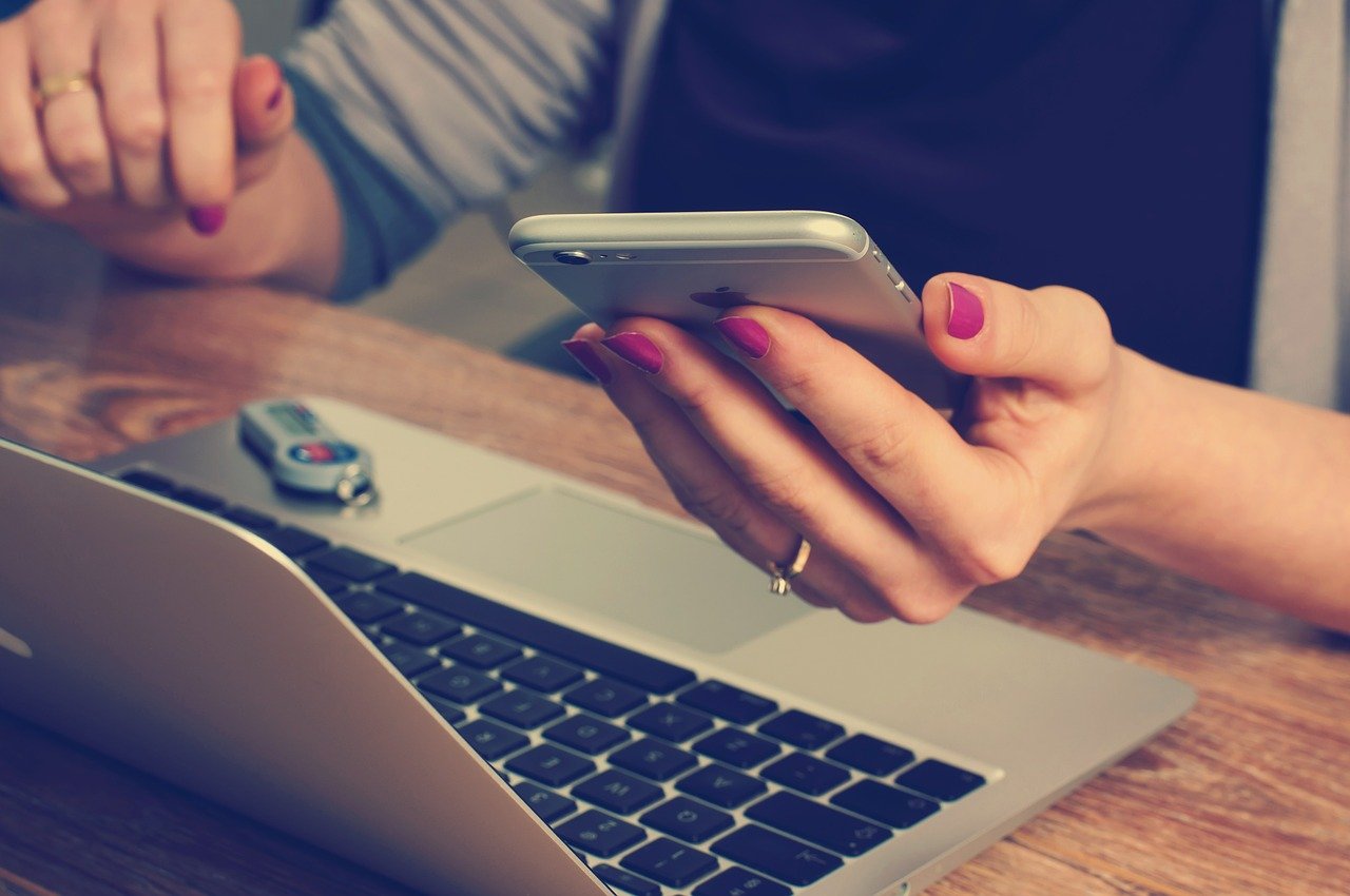 IPO: empresas tem recuo no valor das ações e buscar novos aportes de capital. Imagem genérica mostra mão de mulher com celular e computador, aparentemente fazendo cálculos