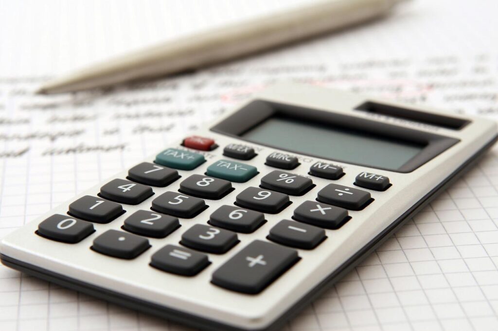 Imagem mostra uma calculadora, uma caneta e um relatório sobre a mesa.