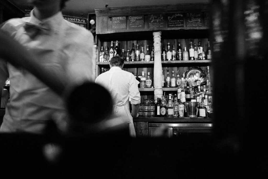 Imagem mostra um bar e um garçom atendendo.