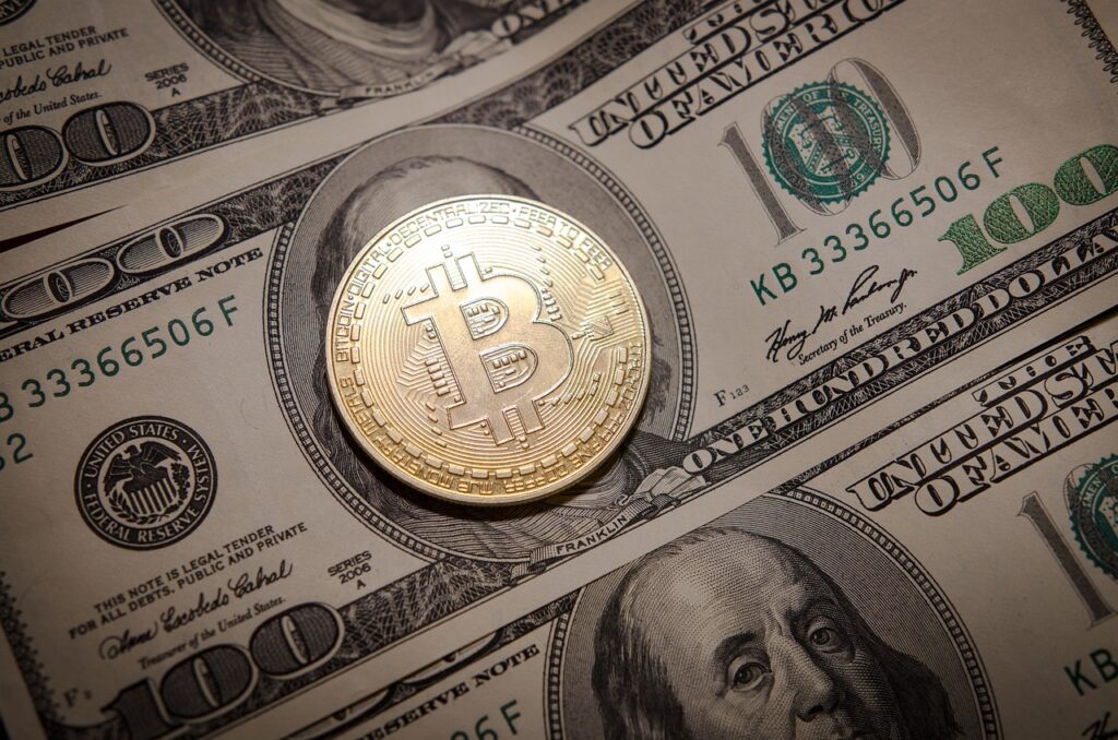 Imagem mostra uma moeda de Bitcoin e uma nota de dólar.