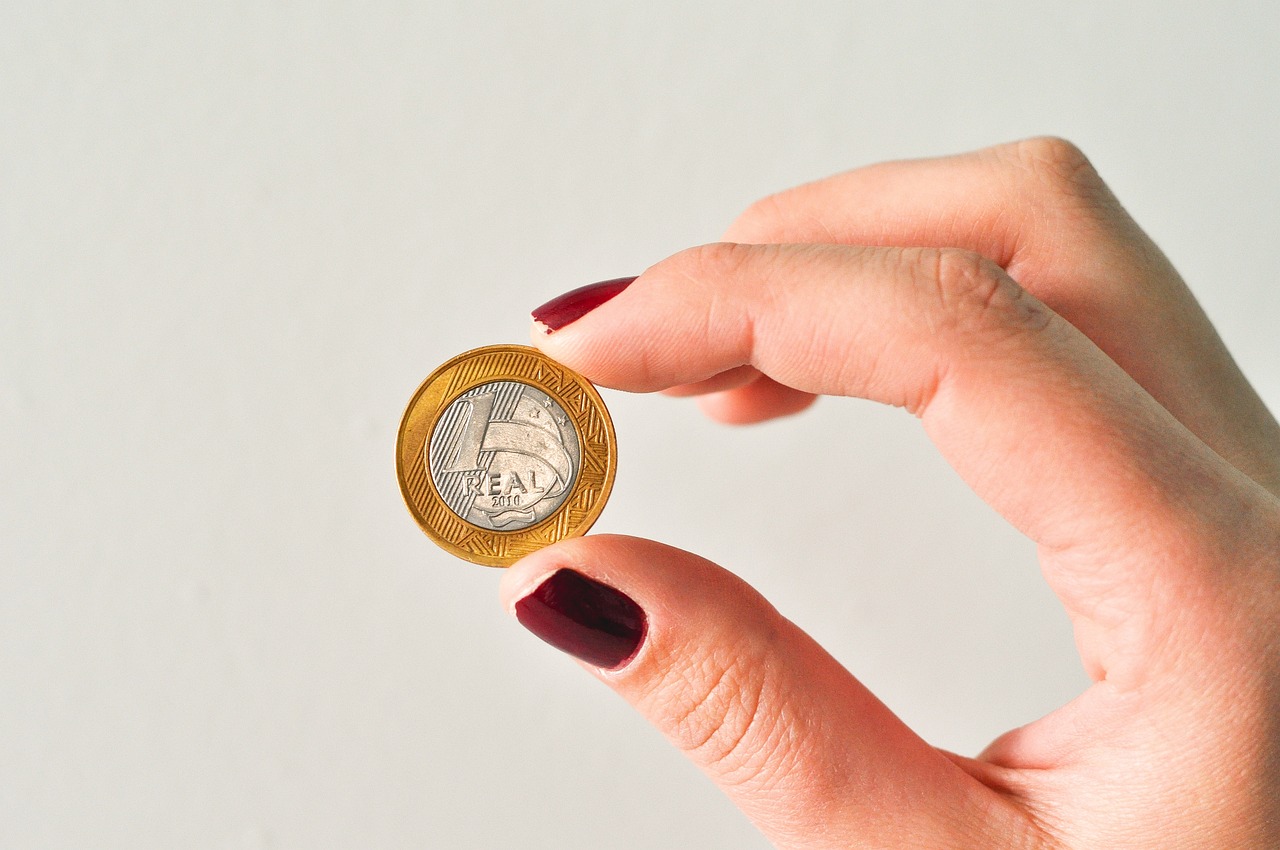 Imagem mostra uma mão feminina segurando uma moeda.