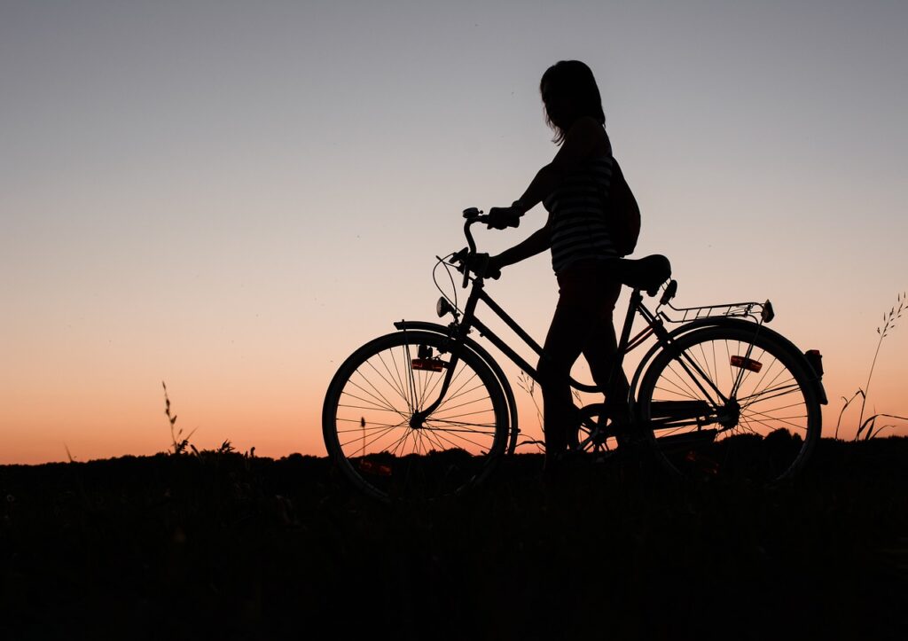 Imagem mostra a silhueta de uma mulher carregando sua bicicleta.