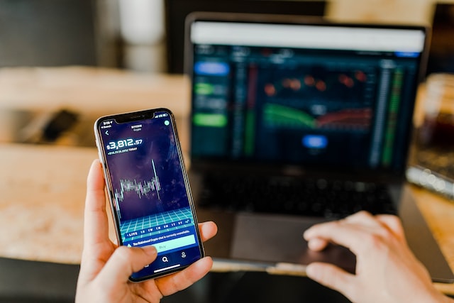 Imagem mostra a mão de uma pessoa segurando um celular e analisando cotação de ação.