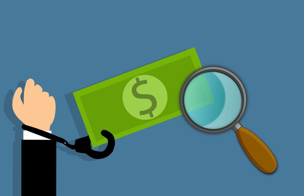 Imagem mostra uma nota de dólar, uma mão algemada a ela e uma lupa.