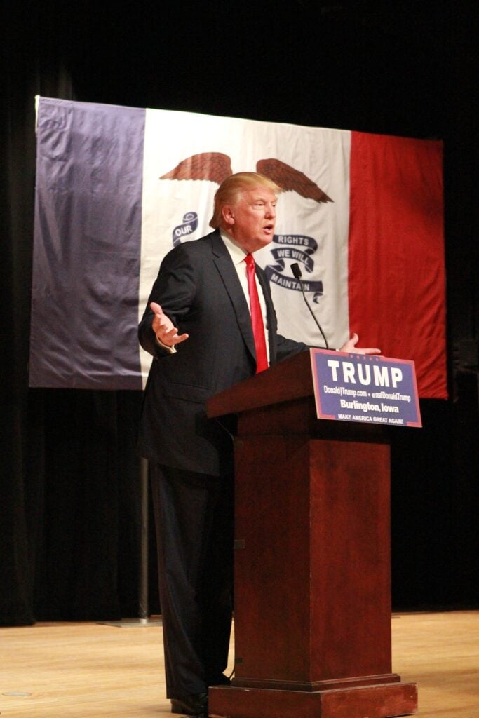 Donald Trump, um homem de meia idade, de cabelo loiro, fala em uma tribuna durante um discurso