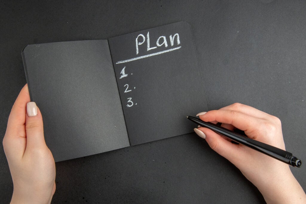 foto de caderno preto, com mão anotando coisas em branco