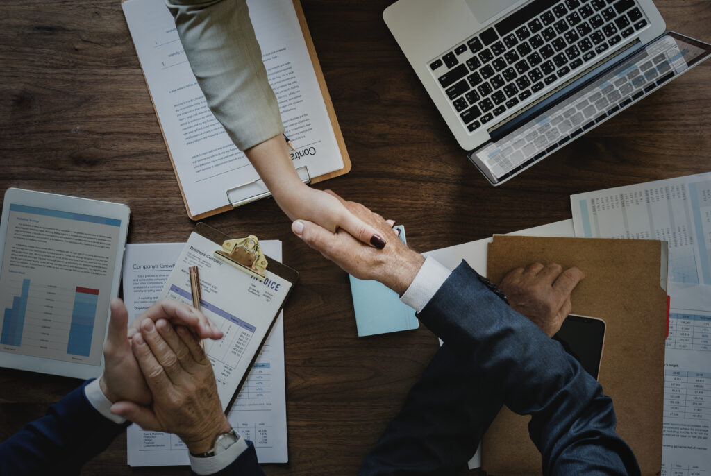 Pessoas se cumprimentando com contratos, computadores. A imagem representa a confiança do negócio.
Fonte: Freepik