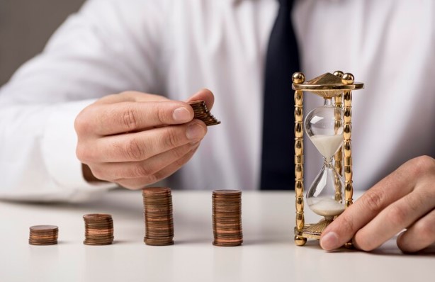 longevidade financeira: homem juntando pilhas de moedas e avaliando ampulheta