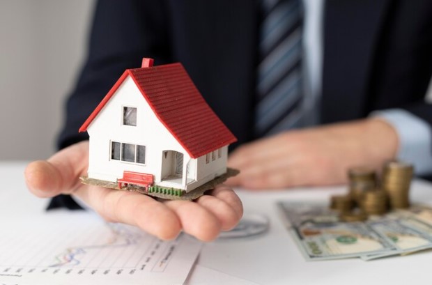 financiamento imobiliário Caixa: imagem de pessoa com moedas e casa de brinquedo na mão