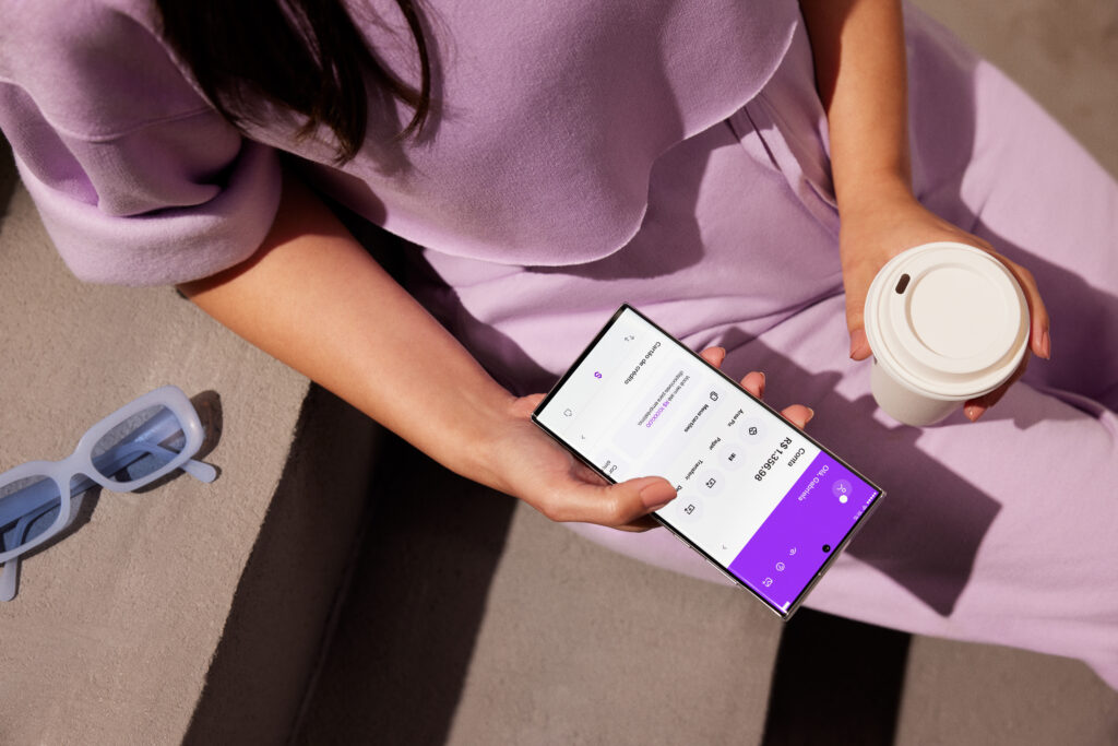 Caixinha do Nubank. Mulher segurando celular com aplicativo do Nubank aberto.
