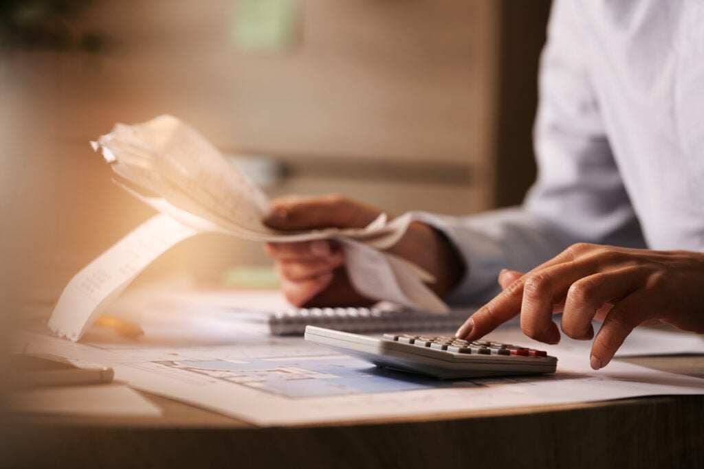 Dedução do Imposto de Renda. Homem fazendo cálculos em calculadora e segurando folhas de papel.