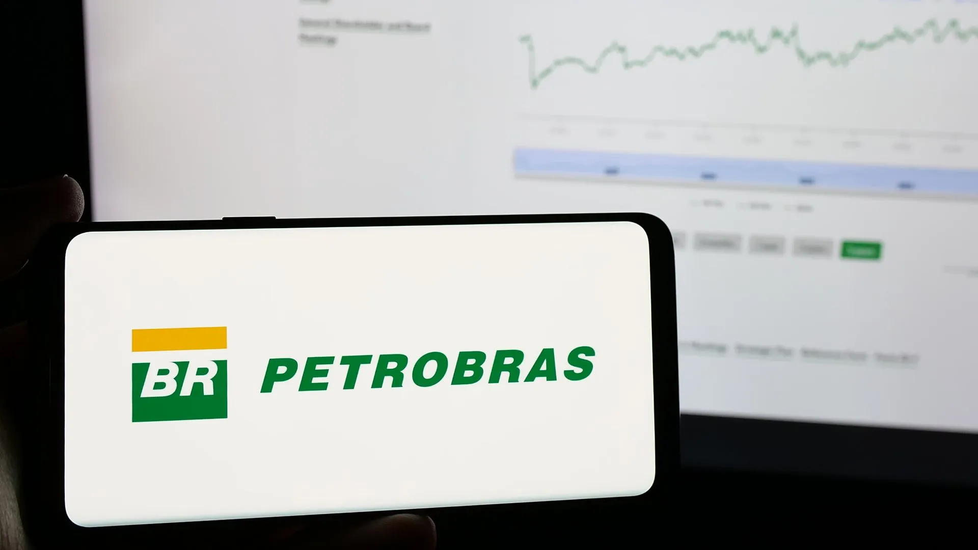 Logo da Petrobras em um smartphone com gráficos financeiros ao fundo, ilustrando a análise de dividendos da Petrobras para 2025.