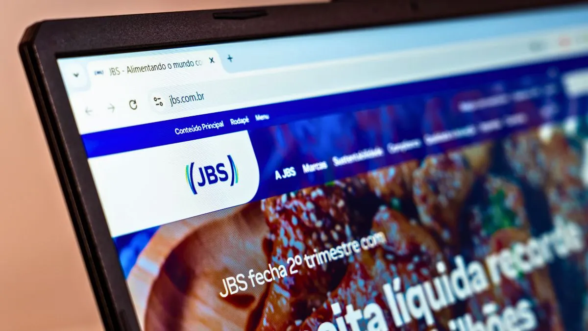 Página web da JBS em laptop, com menção à "receita líquida recorde", simbolizando os dividendos.