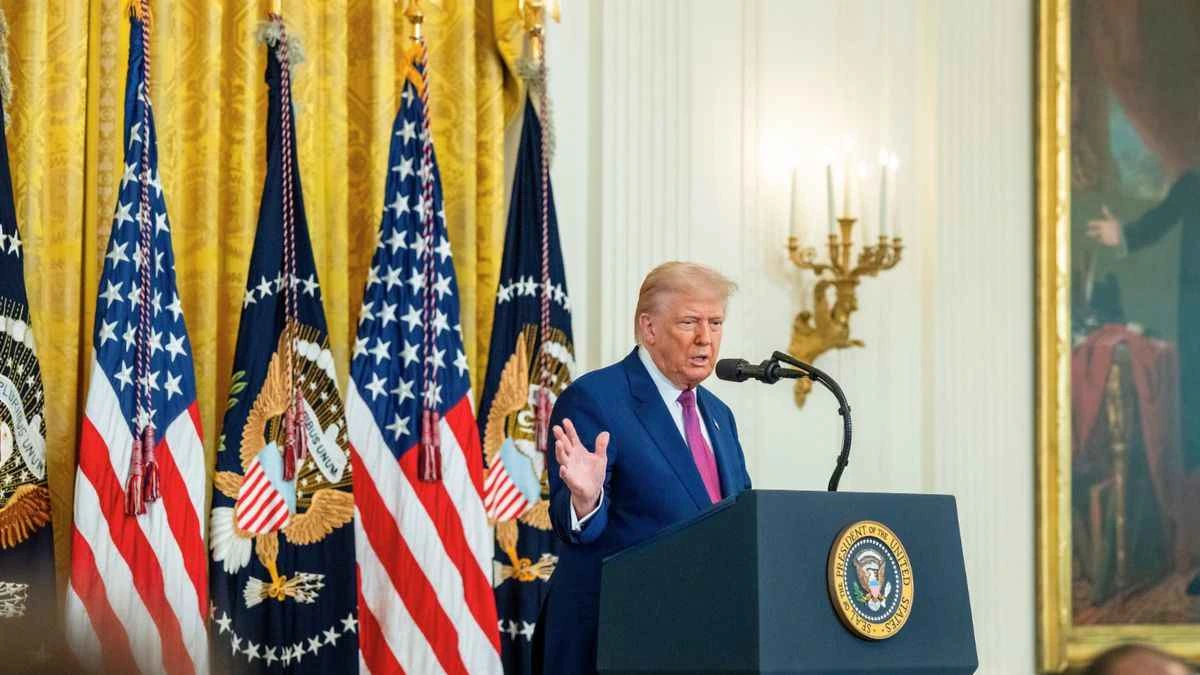 Donald Trump em púlpito com bandeiras dos EUA, anunciando entrevista