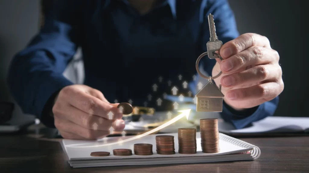 A imagem exibe mãos interagindo com moedas e pilhas de moedas, com um chaveiro de casa e chave. Uma seta ascendente simboliza crescimento financeiro ou imobiliário.