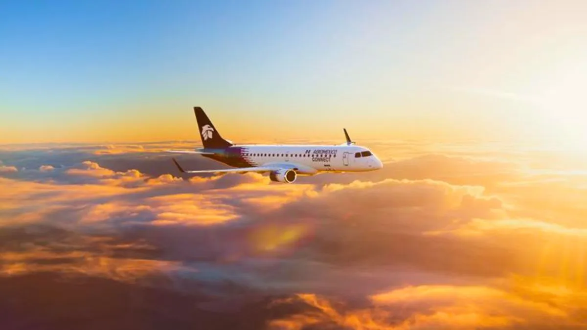 Avião da Embraer voando acima das nuvens com o sol se pondo