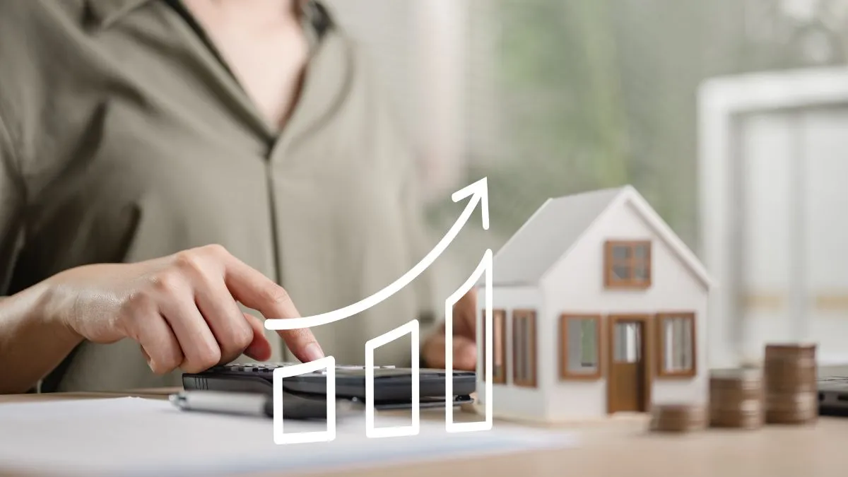 Mãos usando uma calculadora com uma casa em miniatura e um gráfico de crescimento.