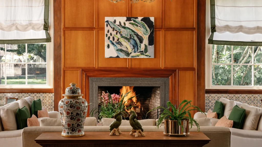 Sala de estar do Hotel das Cataratas com lareira acesa, painéis de madeira, sofás claros, vasos decorativos e janelas com vista para a área verde do Parque Nacional do Iguaçu